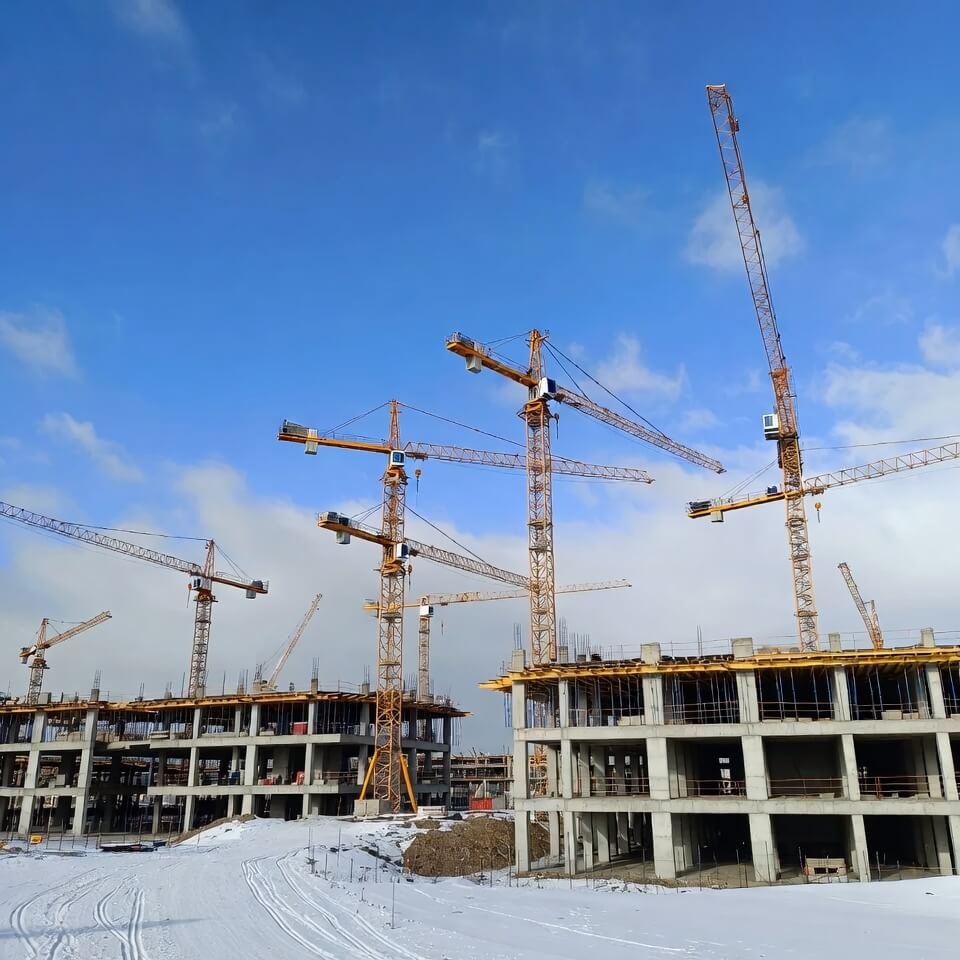 Tall construction cranes over snowy unfinished venue, Milan-Cortina mountains